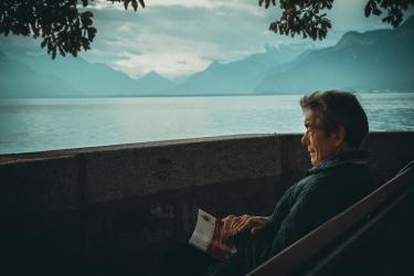 Elderly man sat on a bench next to an alpine lake