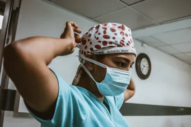 a medical practitioner adjusts their surgical cap, looking intently ahead..