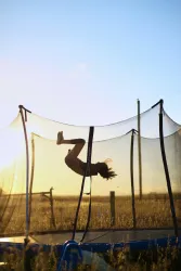 Child performing a flip on a trampoline during sunset in a field.