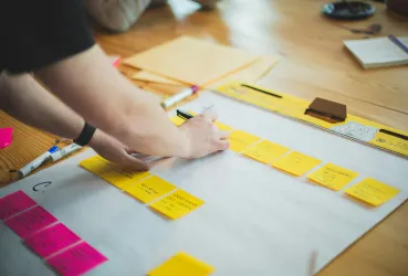 Project planning using sticky notes moved across phases on a clipboard
