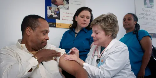 A doctor gives a man a vaccination while onlookers watch