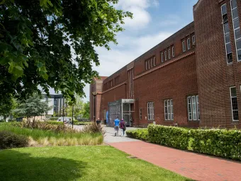 Exterior shot of academic building, trees and grass on a sunny day.