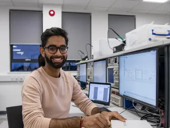 Student smiling to camera at electronics desk.