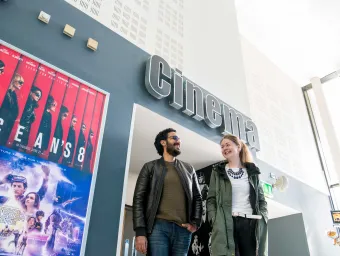 Two students walk underneath a sign reading "cinema". Movie posters adorn the walls.