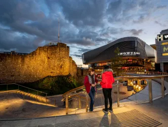 Two students stood on steps overlooking a paved plaza area with large buildings and shops.