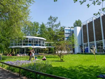 Modern looking campus building with, students relaxing on a grassy area in the foreground.