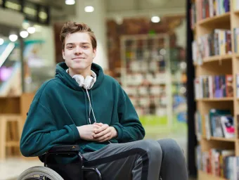 Student in wheelchair looking to camera from library. 