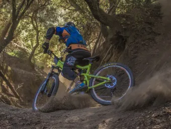 Man on mountain bike, kicking up dirt on a forest bike trail. 
