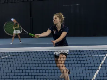 Student playing tennis in indoor sports hall. 