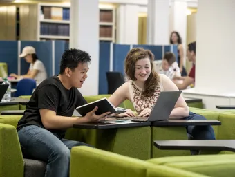 2 students laughing over a laptop in the Hartley Library.