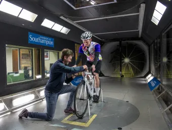 Man on bike in wind tunnel with man adjusting his wheel.