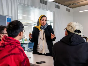 Lecturer talking to 3 students in a classroom. 