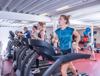 Group of students in gym, running on treadmills surrounded by rowing machines and other gym equipment.