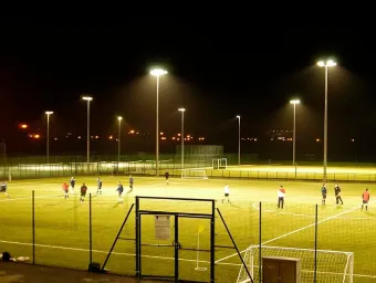 Wide view of floodlit pitches on a dark evening. A group of people are playing football.