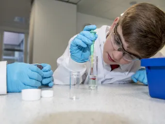 Young school pupil with gloves, goggles and pipette doing experiment in lab