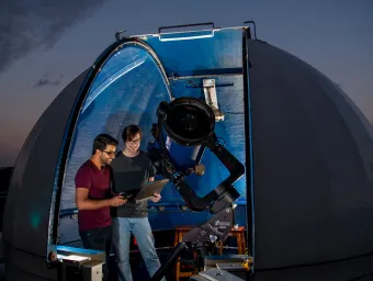 Astronomy students studying data in the shadow of a telescope and rooftop observatory dome.