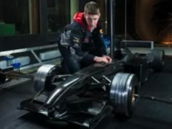 A male student kneeling beside a half-scale model of a Formula 1 car, adjusting various controls.
