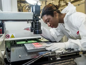 A student wearing protective clothing uses printed electronics and materials equipment