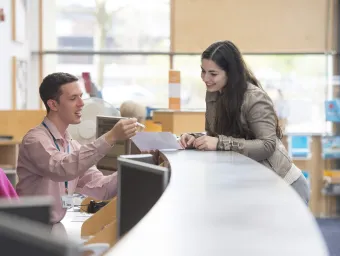 A student leaning over the counter at Student Services as a staff member talks her through a document.