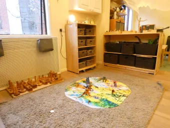 The toddler room at our Early Years Centre. A mat is laid out on the carpet with several model dinosaurs, and more toys in baskets on shelves in the background.