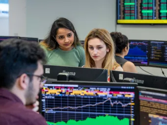 Students sitting at a desk, looking at desktop screens.