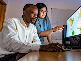 Two researchers stare at a screen which has geographic information about the world.