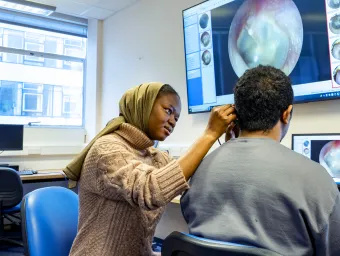 Audiology student looking into a persons ear and showing it on a big screen