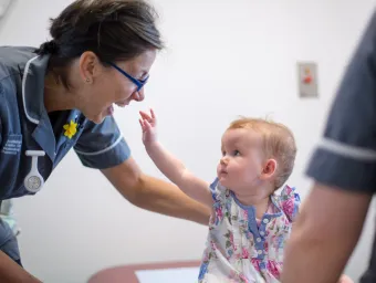 Baby reaches up towards smiling research nurse 