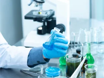 a lab bench with glass equipment and a hand holding a flask with coloured liquid