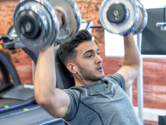 A student lifts weights above his head, he looks determined