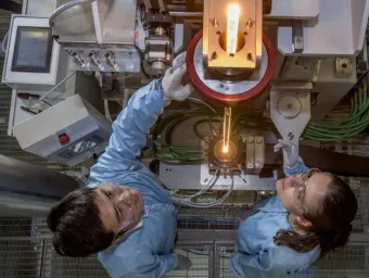 View from above of two researchers feeding glass into a fibre drawing furnace.