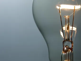 A close up of the inside of a light bulb focuses on the filament of tungsten wire that electricity runs through, a warm, lit colour in contrast to the grey background. Light bulbs are sometimes used as a way to communicate that someone's had a good idea or some insight.