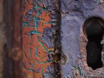 A close up of a key hole in a metal lock that has been weathered  by time
