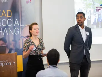 A speaker at a University of Southampton talks to an audience, with a 'Social Impact Lab' slide displayed above them