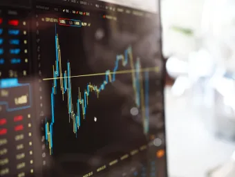 Close up of a computer screen with a dark background showing a stock market graph with peaks and troughs