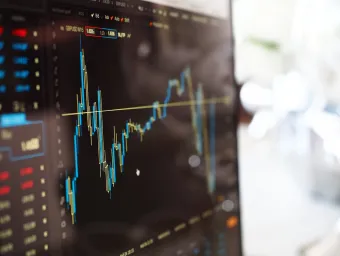 Close up of a computer screen with a dark background showing a stock market graph with peaks and troughs