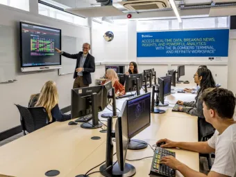 A smiling lecturer leads a small class in the financial laboratory