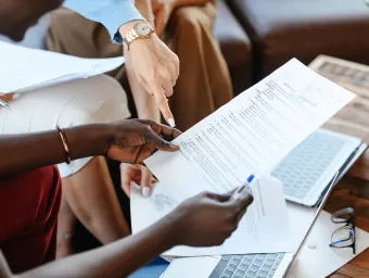 Pexels image showing hands holding a sheet of paper and pen, in a formal meeting