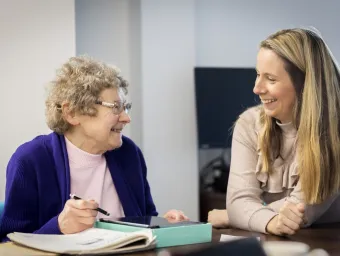 Two women, one younger, one older, smile at each other while sitting at a table