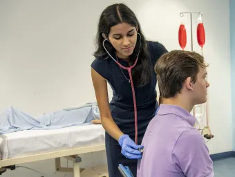 An undergraduate medicine student practices using a stethoscope on a patient in the clinical skills suite