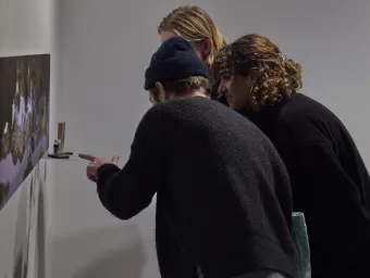 Three gallery visitors lean forward to examine an artwork hanging on the wall at The Winchester Gallery