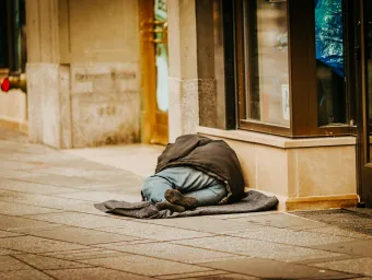 A homeless person lies in the street next to a shop window