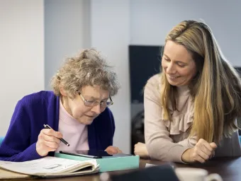 An older woman uses a tablet supported by a younger woman 
