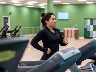 A woman with her hair tied up and earpods running on a treadmil in the gym.