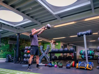A man lifting a dumbell straightout in front of his body. There are lots of weights and equipment behind.