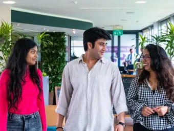 Three students are talking with each other while walking down a bright university campus corridor.