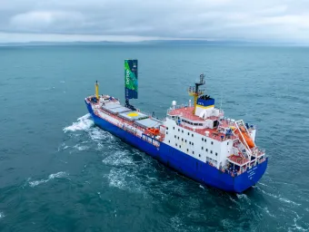 A large cargo vessel sailing on the ocean. It has a 20 metre-high wing sail. 