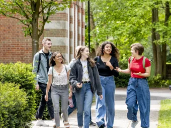 A group of students talking and walking along a path at Avenue campus. The trees are in full leaf and the sun is shining. 