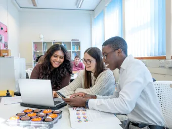 Students smiling looking at a laptop in a classroom.