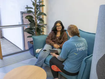 A student discussing support options with a Student Hub advisor while sat on a sofa.